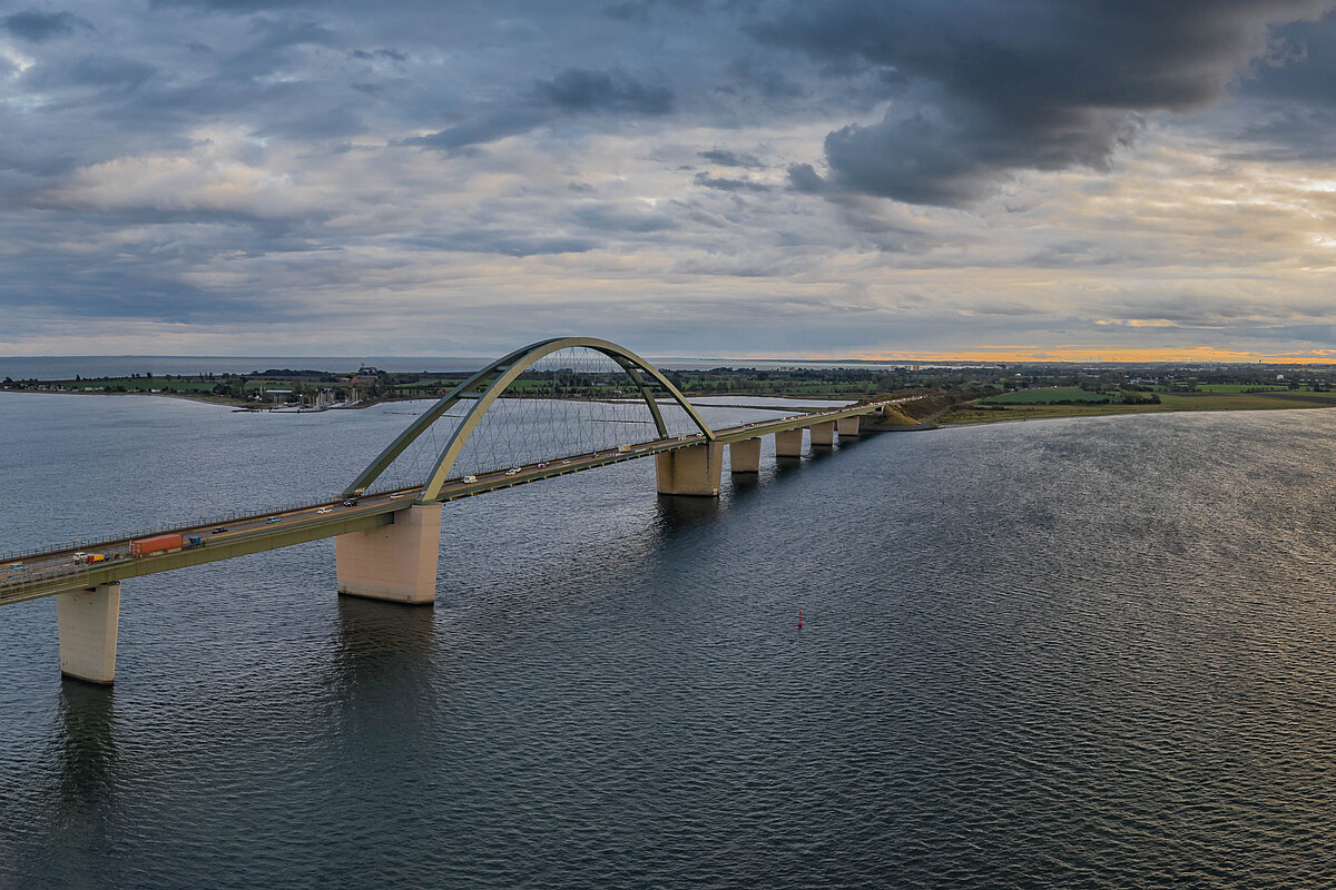 Eine große Bogenbrücke überspannt eine Wasserstraße unter einem bewölkten Himmel