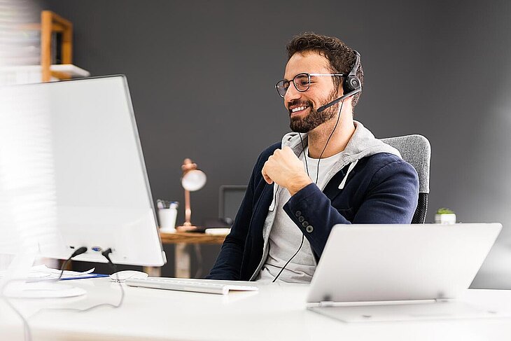 Mann mit Headset schaut lächelnd auf einen Bildschirm