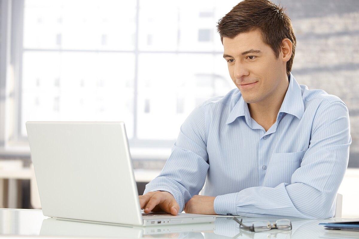 Mann in hellblauem Businesshemd arbeitet an seinem Laptop