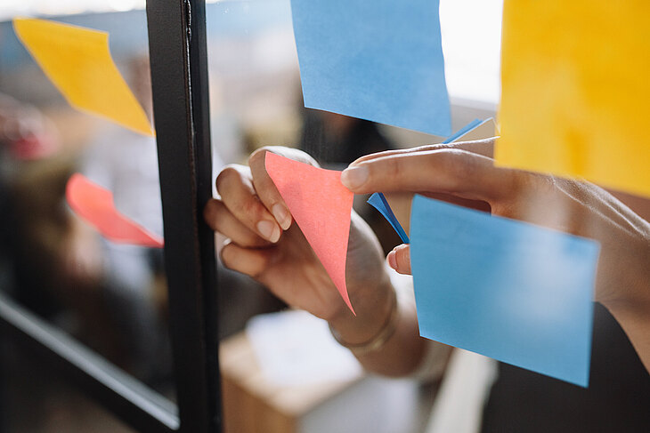 5 Fakten über Ausschreibungen Hände befestigen bunte Haftnotizen an einer Glaswand während eines Meetings