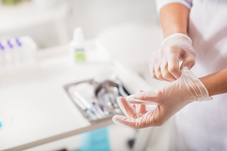 Eine Person zieht in einer medizinischen Umgebung ein Paar durchsichtige Vinyl-Untersuchungshandschuhe an