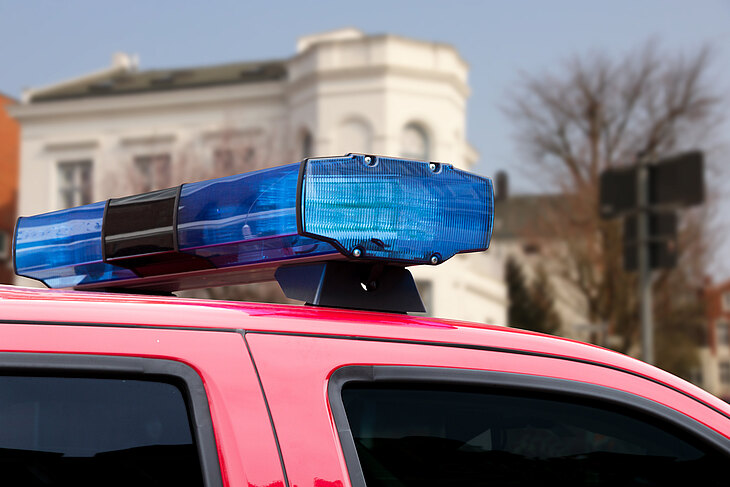Ein blaues Blaulicht auf dem Dach eines roten Feuerwehrfahrzeugs vor einem Gebäude